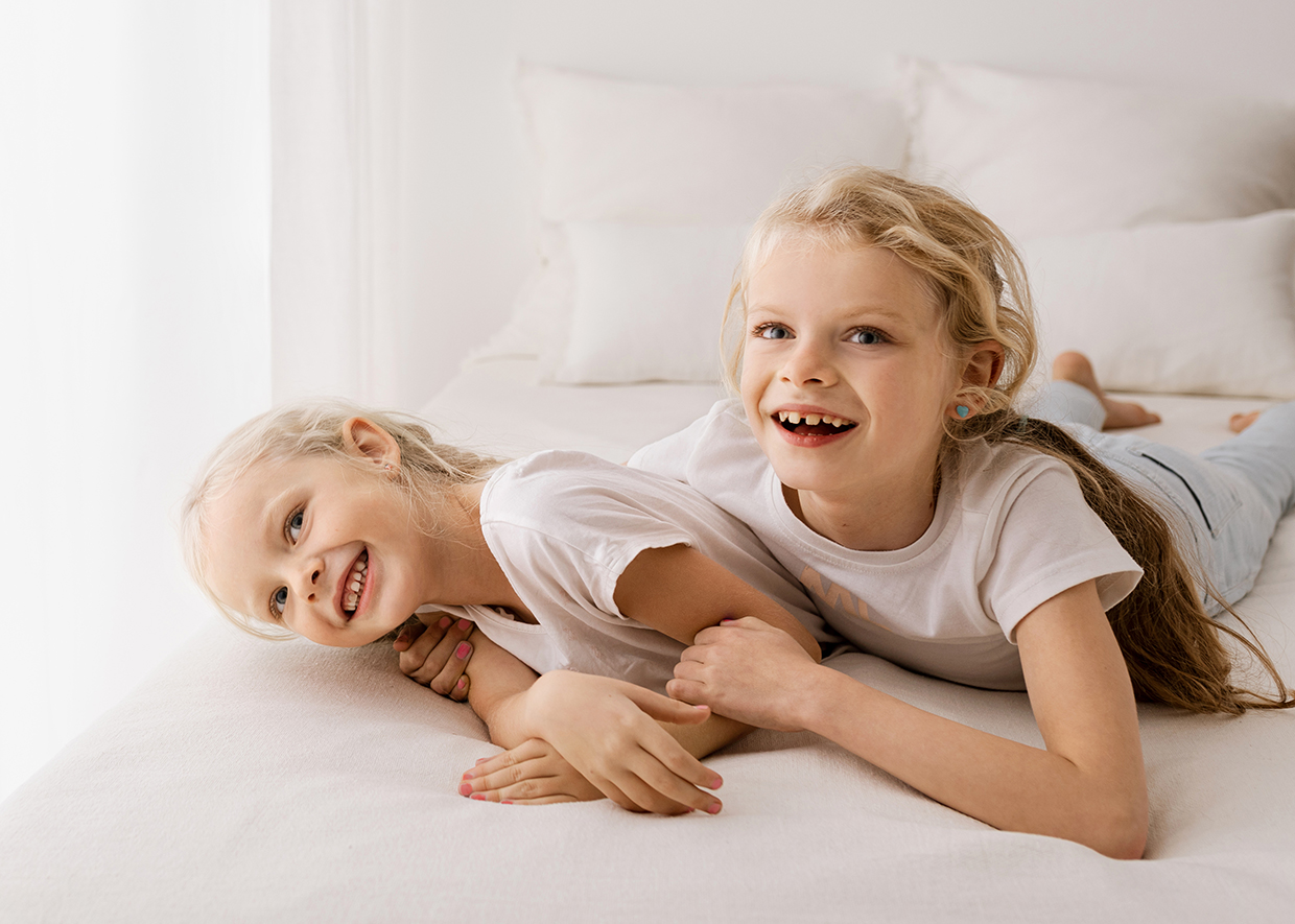 Zwei Geschwister spielen auf dem Bett und lächeln in die Kamera im Rahmen - Kinderfotos Rostock von Kinderfotografin Jenny Schuster