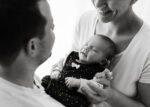 Vater und Mutter halten ihr Baby auf diesem Familienfoto zwischen sich in den Armen und sind überglücklich - Familienfotografie Rostock von Fotografin Jenny Schuster