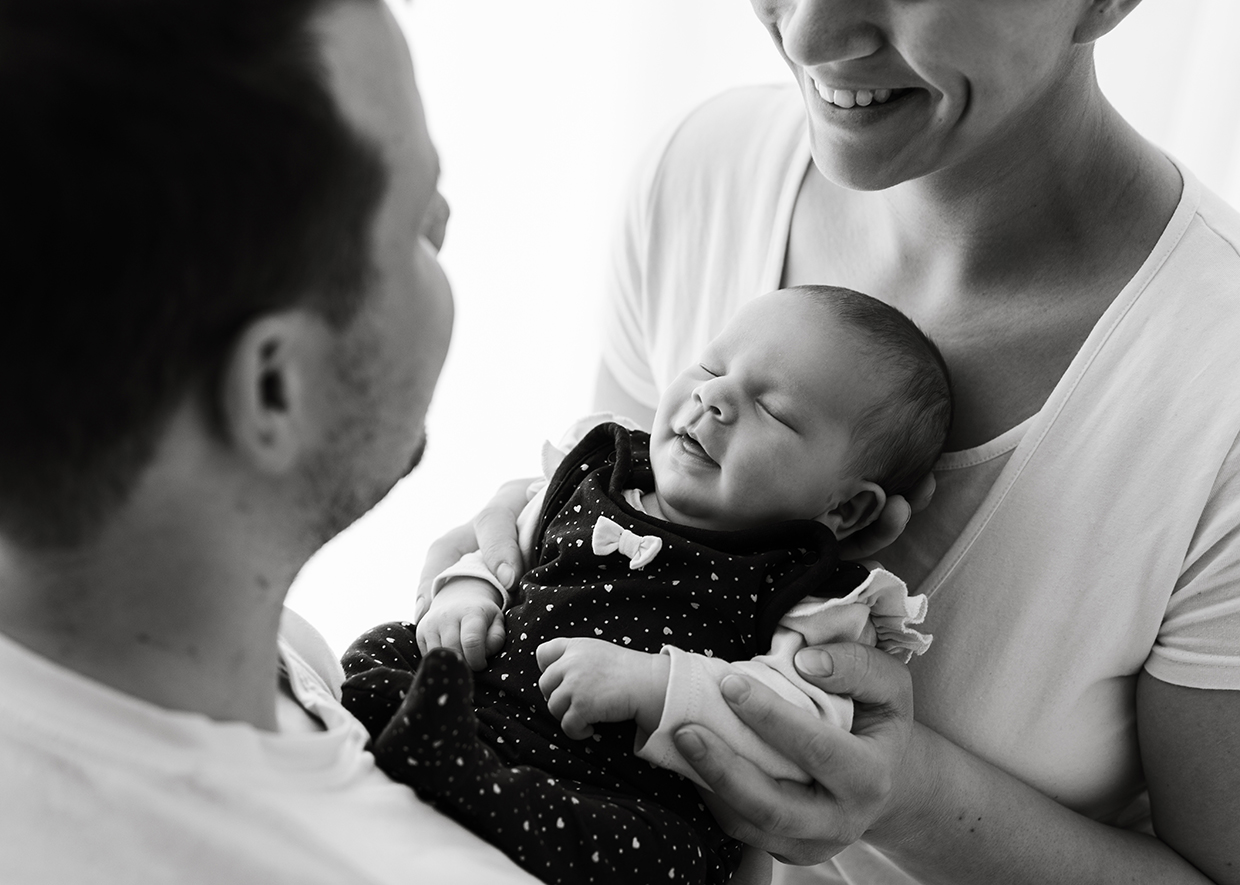 Vater und Mutter halten ihr Baby auf diesem Familienfoto zwischen sich in den Armen und sind überglücklich - Familienfotografie Rostock von Fotografin Jenny Schuster