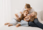 Mutter kuschelt mit ihren zwei Töchtern glücklich und lachend auf dem Sofa beim Familien-Fotoshooting in Rostock mit Familienfotografin Jenny Schuster