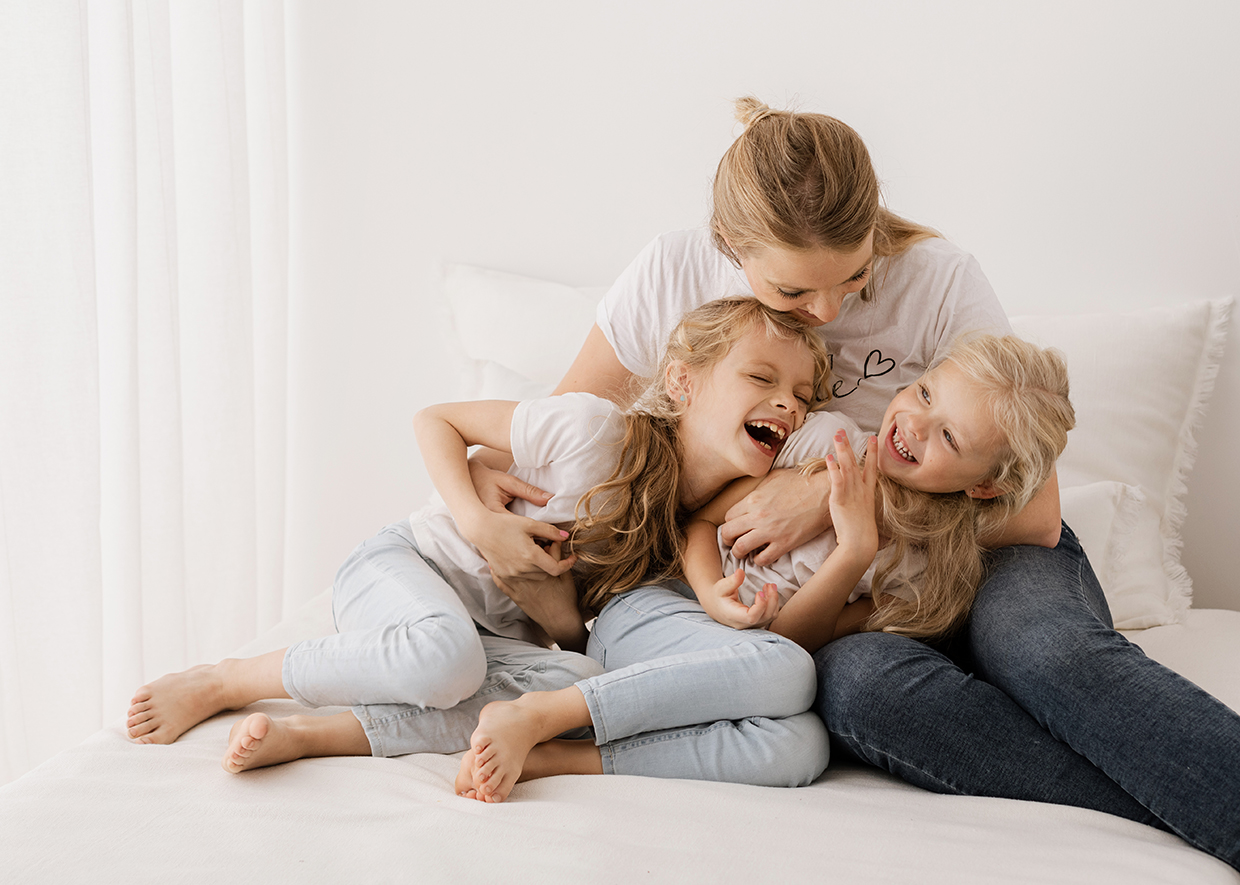 Mutter kuschelt mit ihren zwei Töchtern glücklich und lachend auf dem Sofa beim Familien-Fotoshooting in Rostock mit Familienfotografin Jenny Schuster